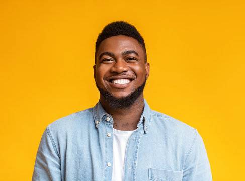 Smiling man with short hair and a beard, wearing a denim shirt, set against a vibrant yellow background, representing customer satisfaction.