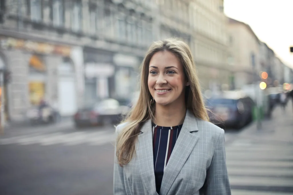 Confident young woman in a stylish suit smiles on a city street, embodying professionalism and urban charm, perfect for a business profile.